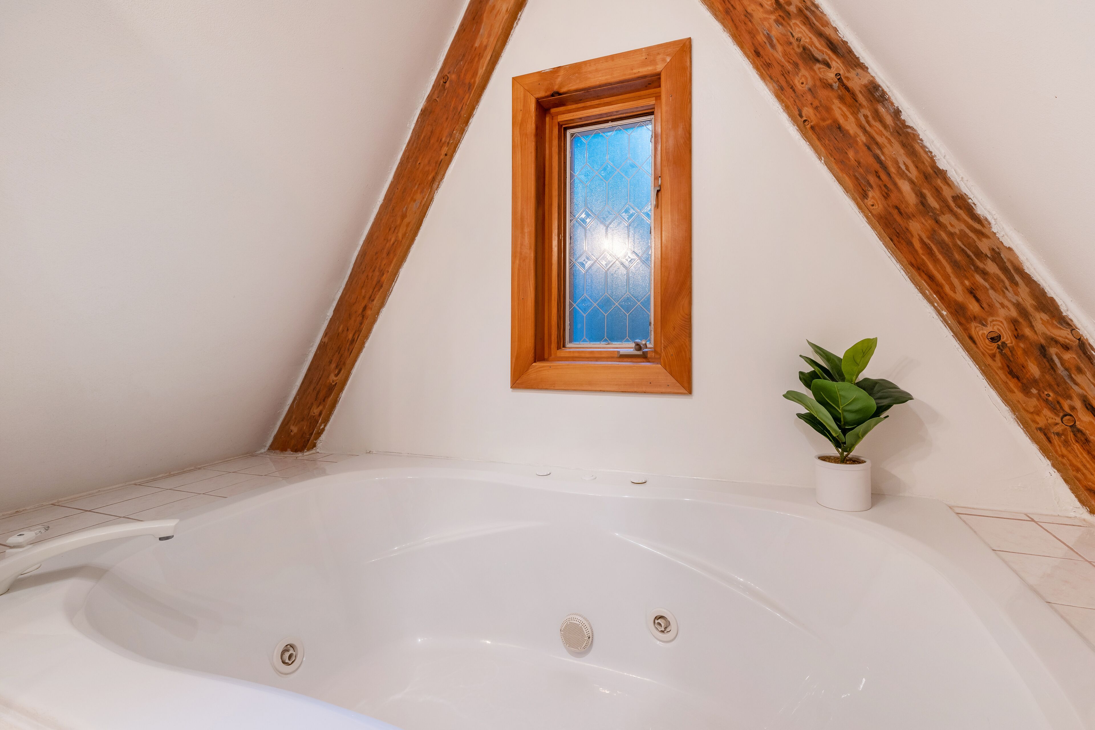 A room with a white bathtub, a wooden window frame, and a potted plant.