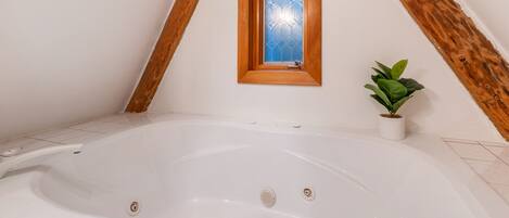 A room with a white bathtub, a wooden window frame, and a potted plant.