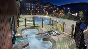 A hot tub area with a wooden fence, a pool, and a building in the background. - Log Cabin with Private Indoor Heated Pool-Hot Tub-firepit-Game Room-100 acres (Homer)