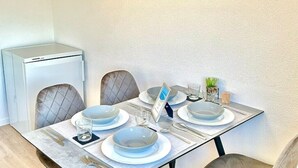 A dining area with a table set for four, including plates, cutlery, and glasses. There is a small refrigerator to the left and a plant on the table. - Diamond Apartments: Dreiländereck Nahe Flughafen (Rheinfelden (Baden))