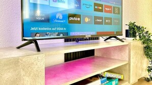 A flat-screen TV mounted on a wooden stand with a colorful interface displaying various streaming services. - Diamond Apartments: Dreiländereck Nahe Flughafen (Rheinfelden (Baden))
