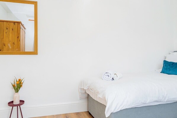 Un dormitorio con cama, una mesita con un jarrón de flores y un espejo en la pared.