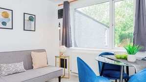 Una sala moderna con un sofá gris, sillas azules, una mesita redonda y una ventana con cortinas.
