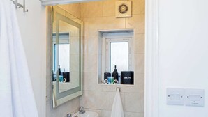 A modern bathroom with a large mirror, a sink, a towel rack, and a small shelf with toiletries.