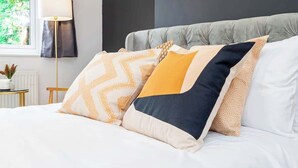 A neatly made bed with a grey upholstered headboard, white bedding, and decorative pillows in various patterns and colors.