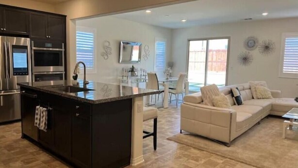 A modern kitchen with a central island, stainless steel appliances, and a dining area with a white table and chairs. - Charming 4BR/3BA Home in Menifee (Menifee)
