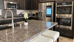 A modern kitchen with dark cabinets, stainless steel appliances, a granite countertop, and a small white bench. - Charming 4BR/3BA Home in Menifee (Menifee)