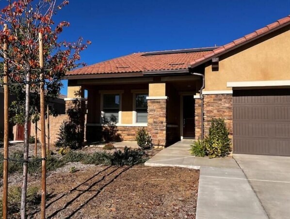 A residential building with a tiled roof, stone facade, and a garage. - Charming 4BR/3BA Home in Menifee (Menifee)