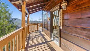 A wooden deck with a glass door leading to a room, overlooking a scenic landscape. - *Spacious 4BD Lodge w/ HOT TUB! Pool + Mtn Views!* (Sevierville)