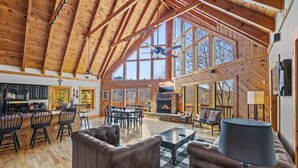 A spacious living area with a high ceiling, wooden beams, a fireplace, and a large window overlooking a scenic landscape. - *Spacious 4BD Lodge w/ HOT TUB! Pool + Mtn Views!* (Sevierville)