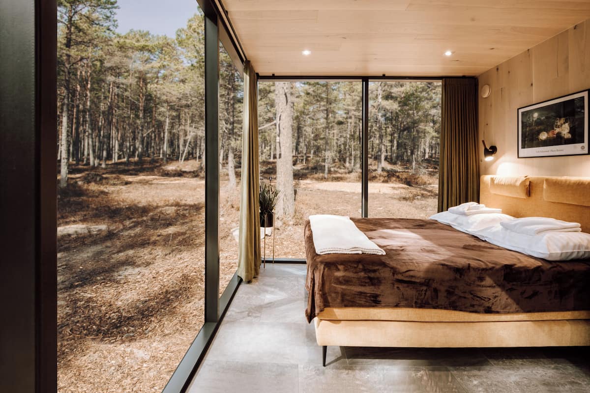 Et soveværelse med en stor seng, udsigt til en skov og et moderne design.