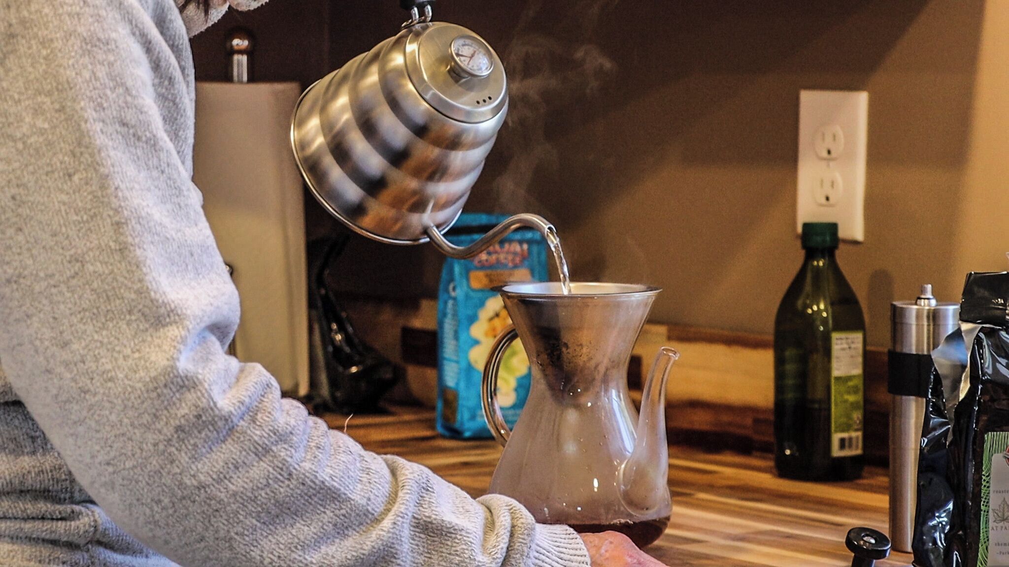 A person pouring water from a kettle into a glass carafe.