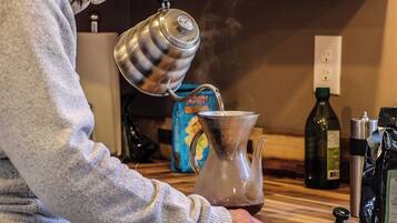 A person pouring water from a kettle into a glass carafe.