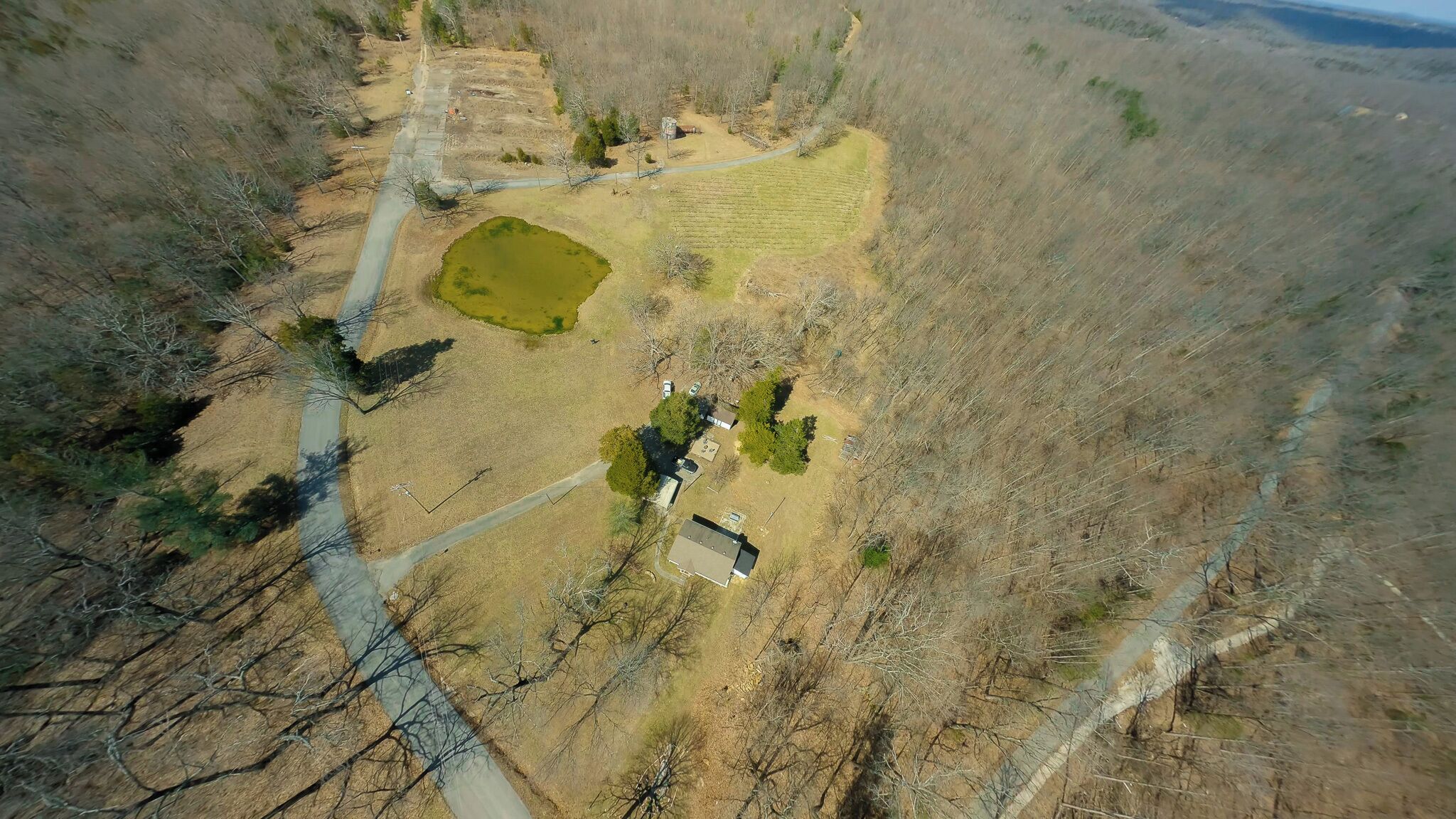 Vue aérienne d’une propriété rurale avec un étang, une petite maison et une zone délimitée par une clôture.