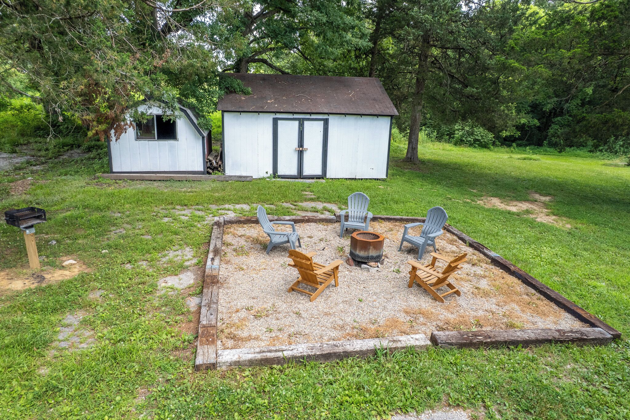 A backyard with a small shed, a fire pit, and four Adirondack chairs arranged around it.