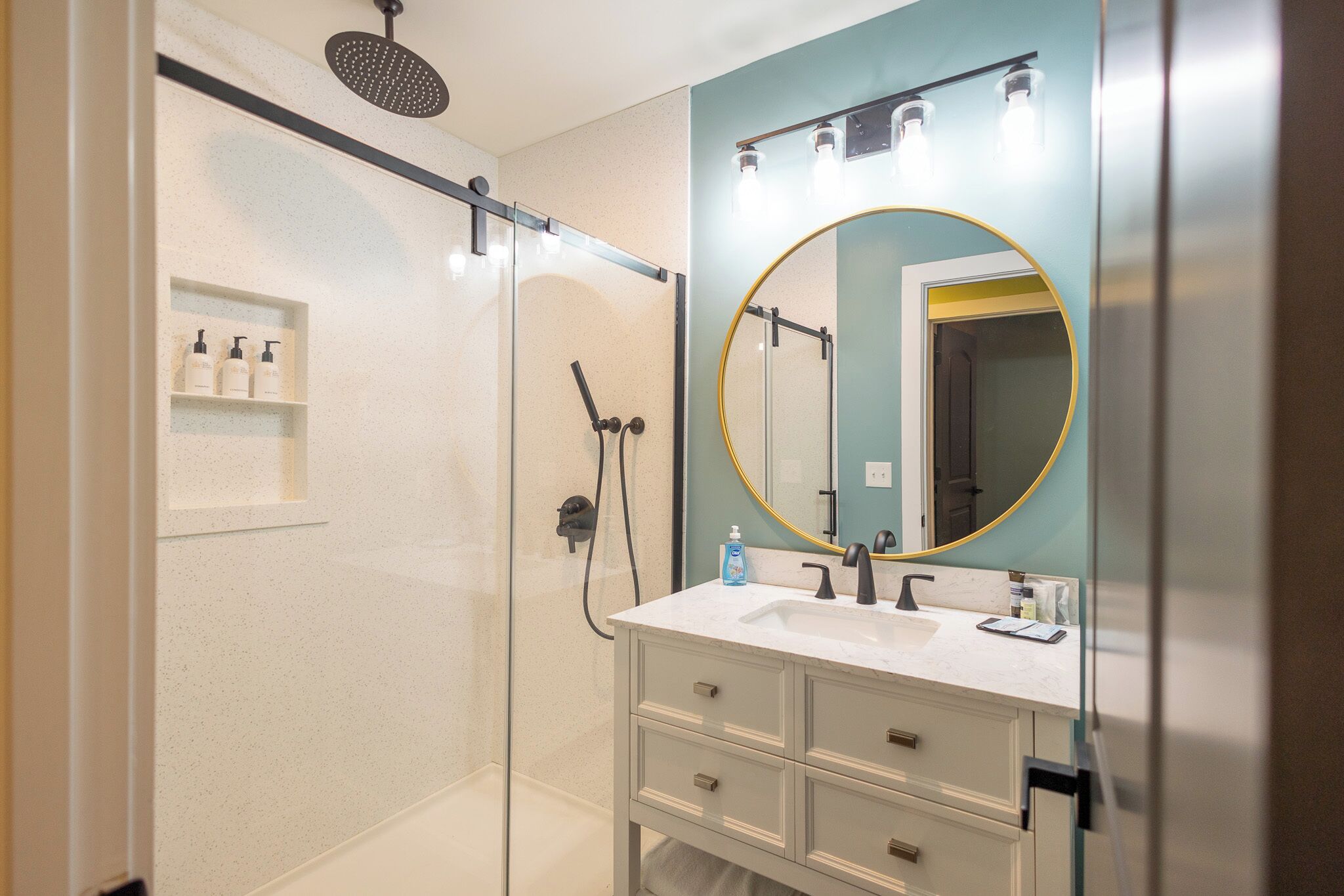 A modern bathroom with a glass-enclosed shower, a white vanity with a gold-framed mirror, and a light blue accent wall.