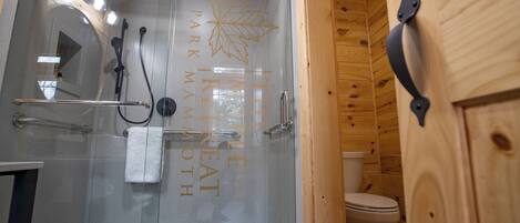 A glass-enclosed shower with a white bathtub, a towel rack, and a toilet in a wooden cabin-style bathroom.