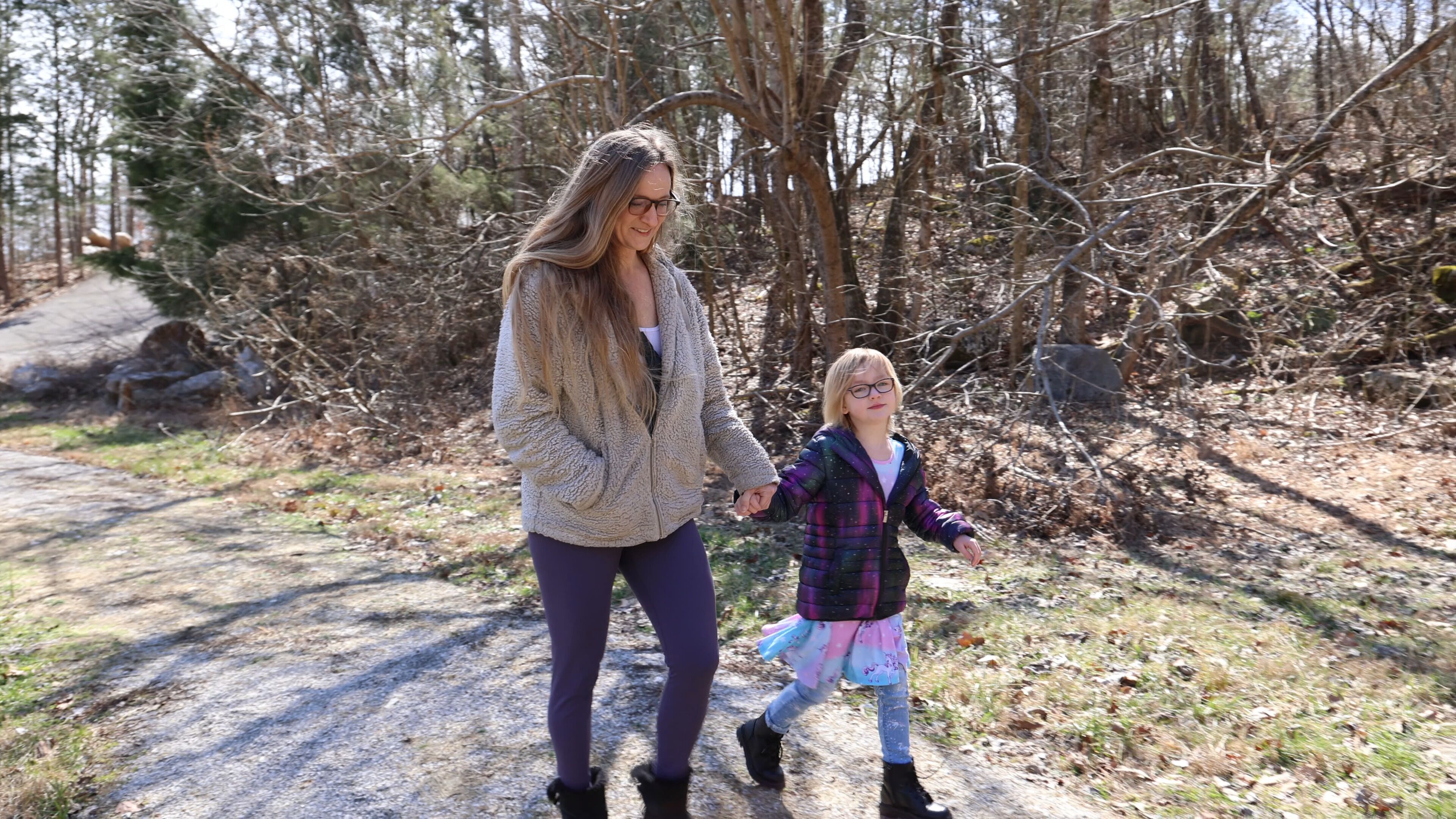 A woman and a child walking on a forest path.