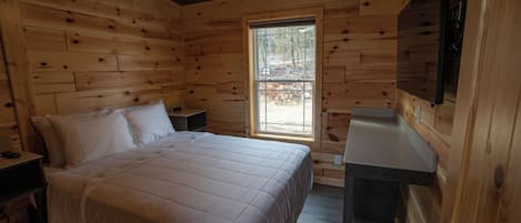 A wooden cabin bedroom with a bed, nightstands, a window, and a mounted TV.