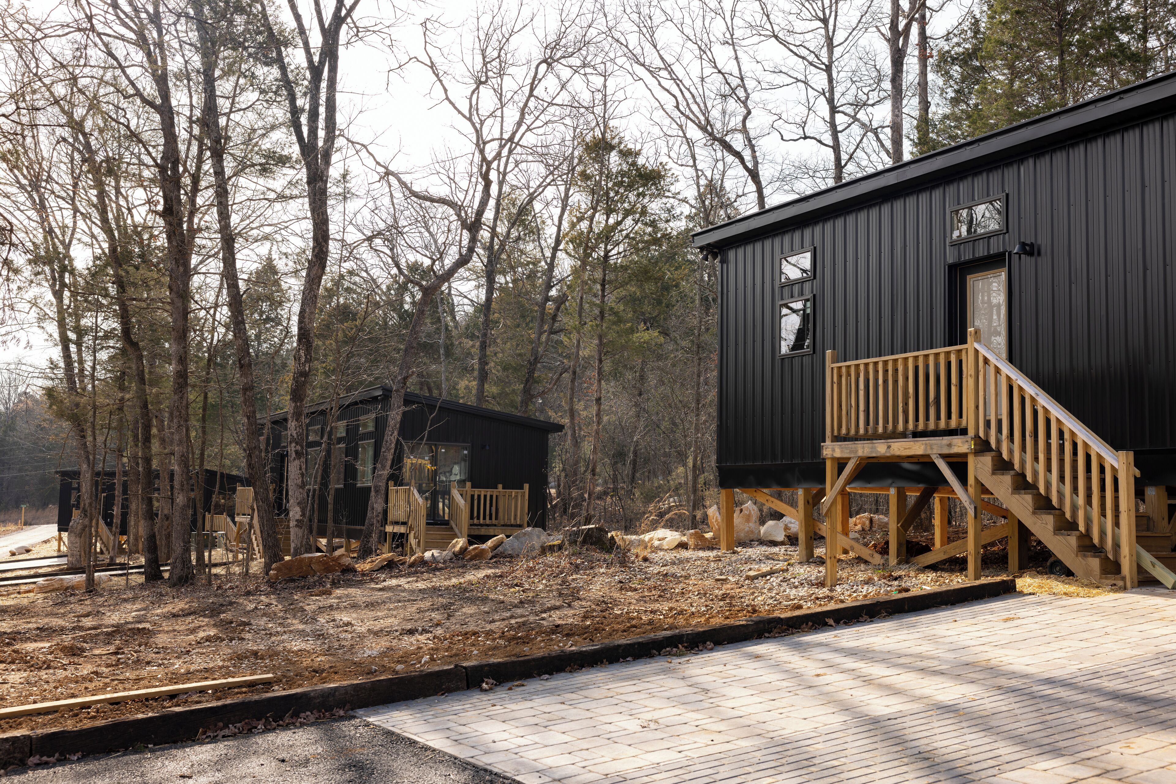 Un bâtiment noir avec un escalier en bois et une terrasse, entouré d’arbres.