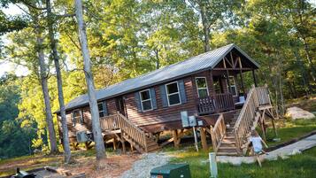 A rustic cabin with a porch, wooden stairs, and a grill area.