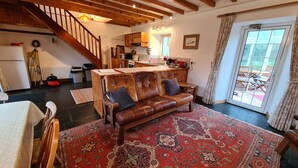 Una sala de estar acogedora con un sofá de cuero, una mesa de comedor y una zona de cocina con armarios de madera y una escalera.