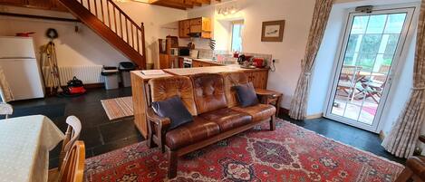 A cozy living room with a leather sofa, a dining table, and a kitchen area with wooden cabinets and a staircase.