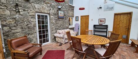 A cozy patio area with a stone wall, a wooden table with chairs, a leather sofa, and a red rug.