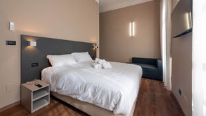 Une chambre d’hôtel moderne dotée d’un grand lit, de tables de chevet, d’un téléviseur à écran plat et d’un canapé.