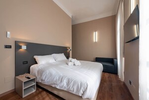 Ein modernes Hotelzimmer mit einem großen Bett, Nachttischen, einem Flachbildfernseher und einem Sofa.