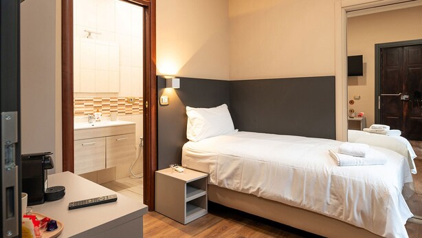 A hotel room with a bed, bedside table, and a bathroom visible through an open door. - Torino Station Relais (Turin)