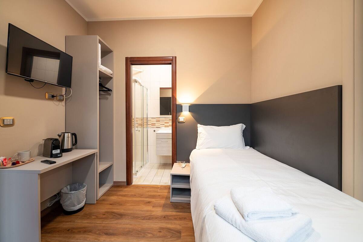 A hotel room with a bed, a desk with a coffee maker, a TV, and a shower area.