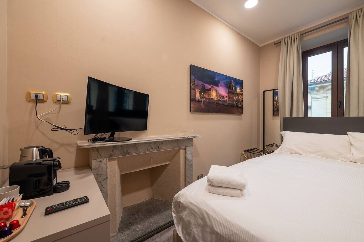 A hotel room with a bed, a TV, a fireplace, a coffee maker, and a window with curtains.
