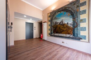 Un pasillo con piso de madera, una puerta azul y un mural de un paisaje con montañas y un río.
