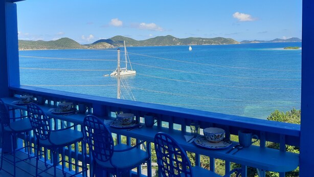 Una mesa con sillas y vistas al mar, con un velero.