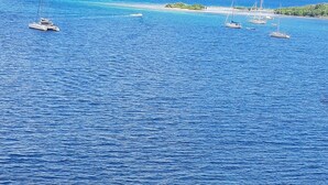Paisaje costero con aguas azul cristalino, varios veleros y accidentes geográficos a lo lejos.