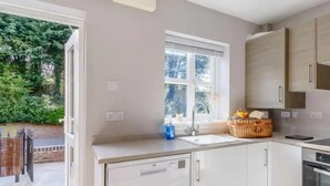 A modern kitchen with white cabinets, a built-in oven, and a window overlooking a garden. - Stunning 2-bed House in Walkington Near Beverley (Beverley)