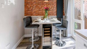 A modern kitchen with a brick wall backsplash, a dining table with two bar stools, and a hanging pendant light. - Stunning 2-bed House in Walkington Near Beverley (Beverley)