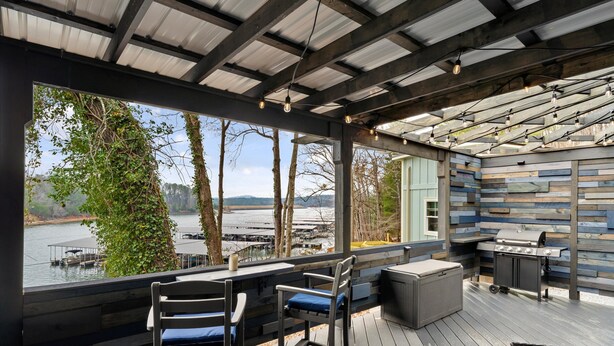 Une terrasse extérieure avec vue sur un lac, du mobilier en bois et un espace barbecue.