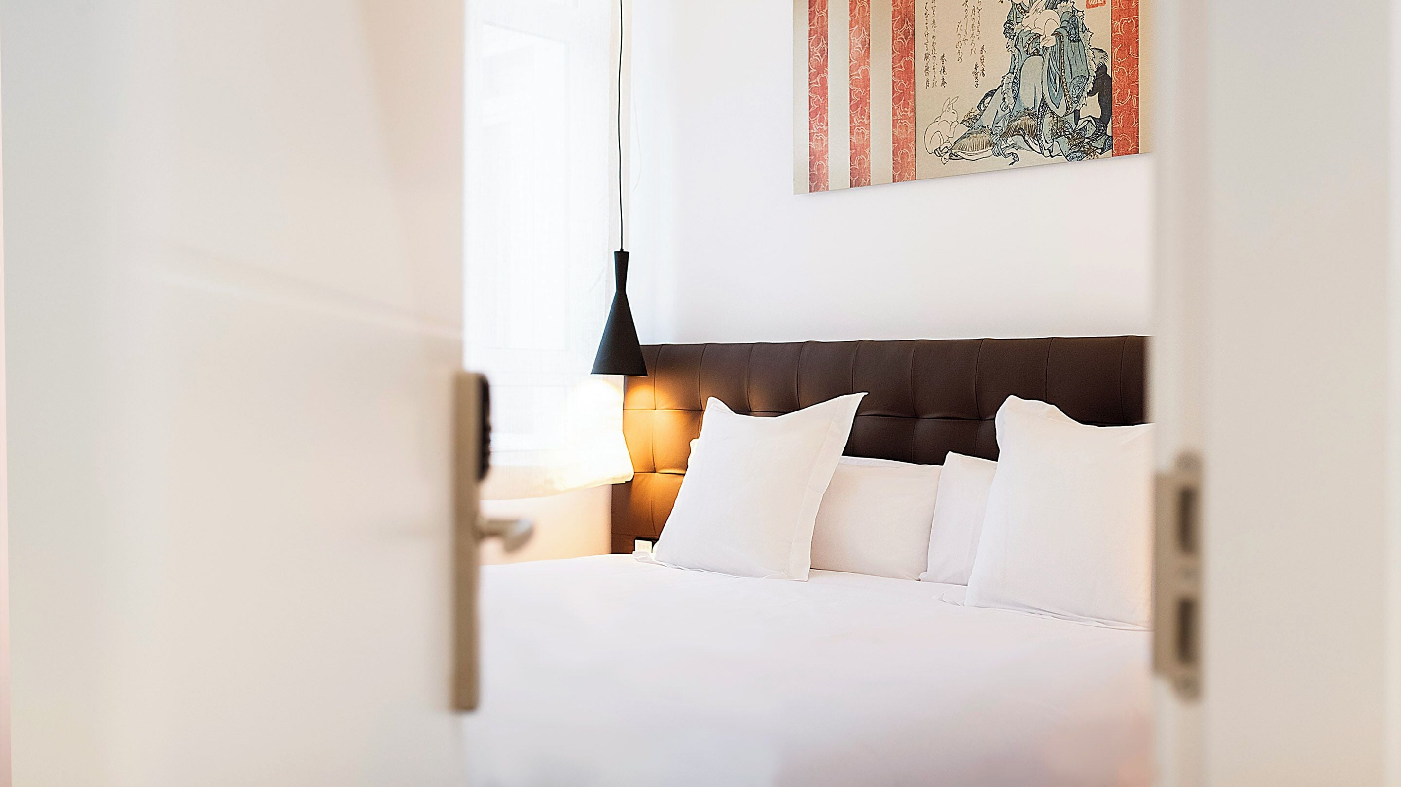A hotel room with a neatly made bed, a dark headboard, and a wall-mounted artwork.