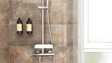 A shower area with a chrome faucet and a handheld showerhead. Two bottles of hair conditioner are mounted on the wall.
