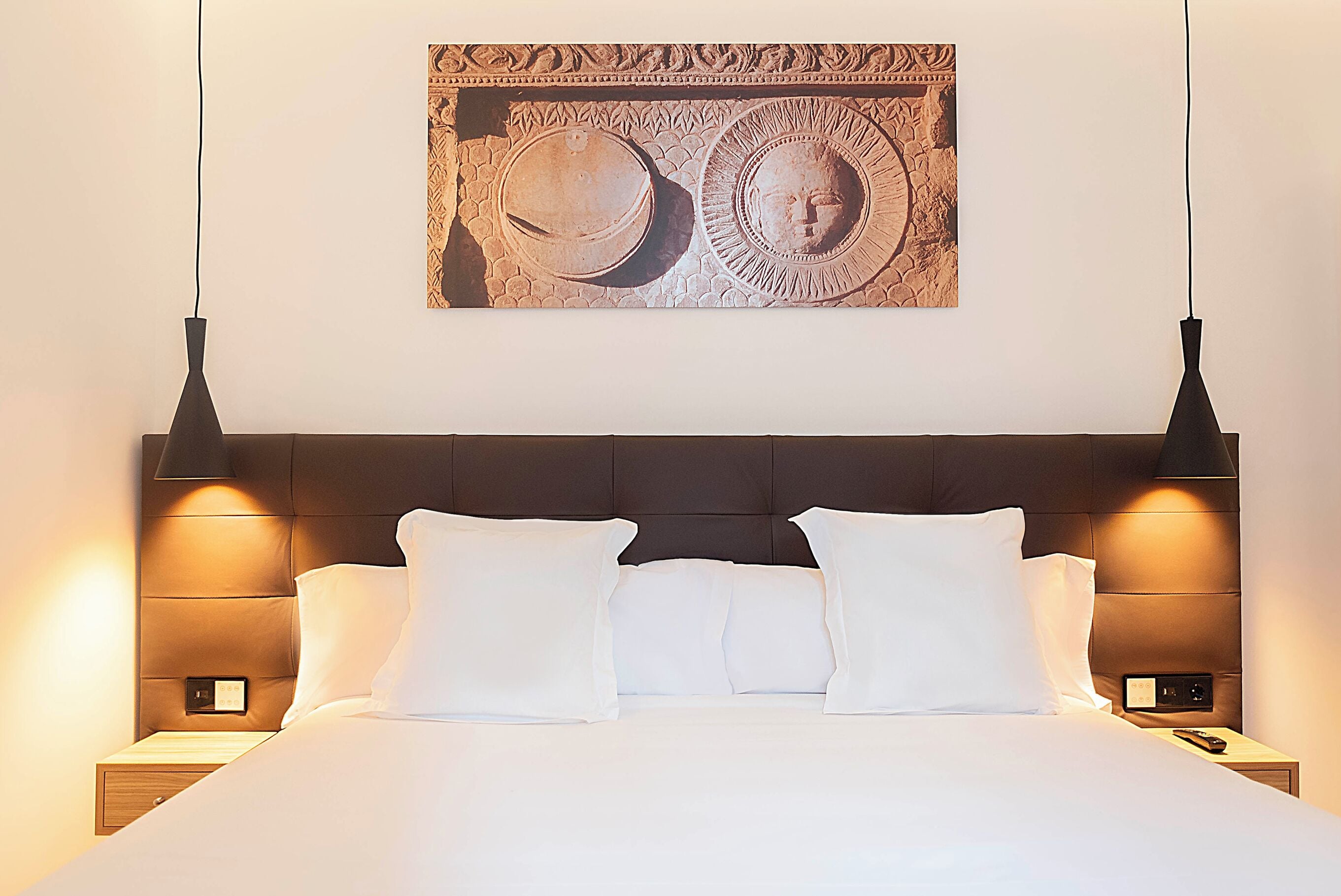 A neatly made bed with white linens and pillows, a dark headboard, and two bedside lamps.