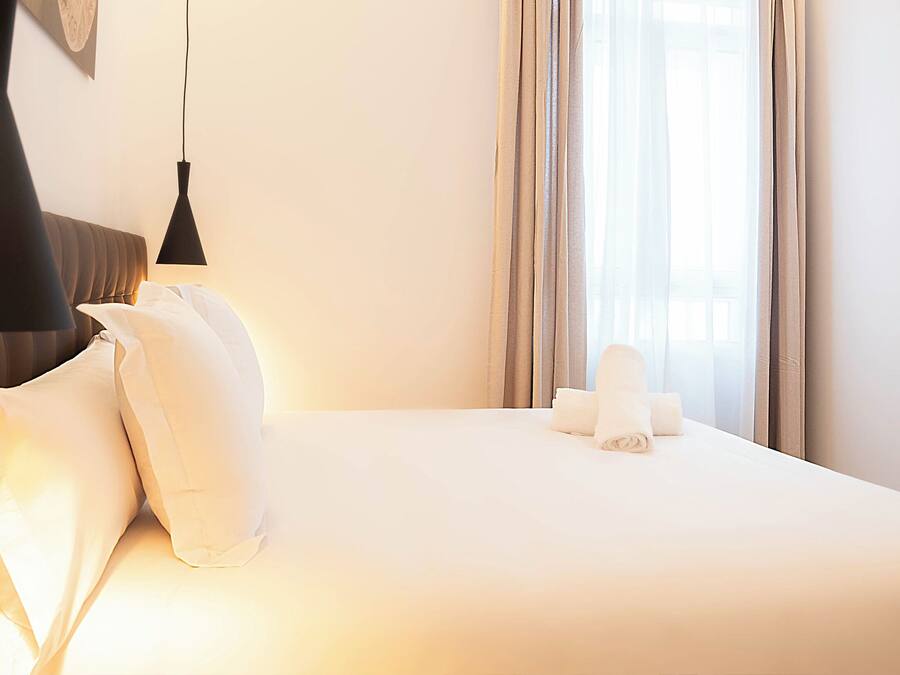 Habitación de hotel con una cama bien hecha, una lámpara colgante y vistas al exterior a través de la ventana.