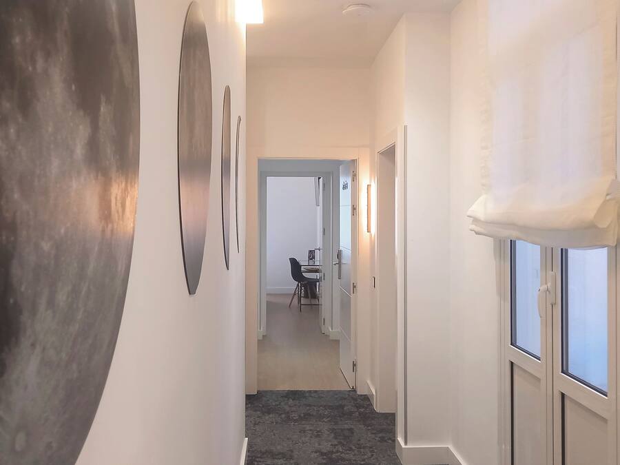 A hallway with a dark floor, white walls, and a door leading to a dining area.