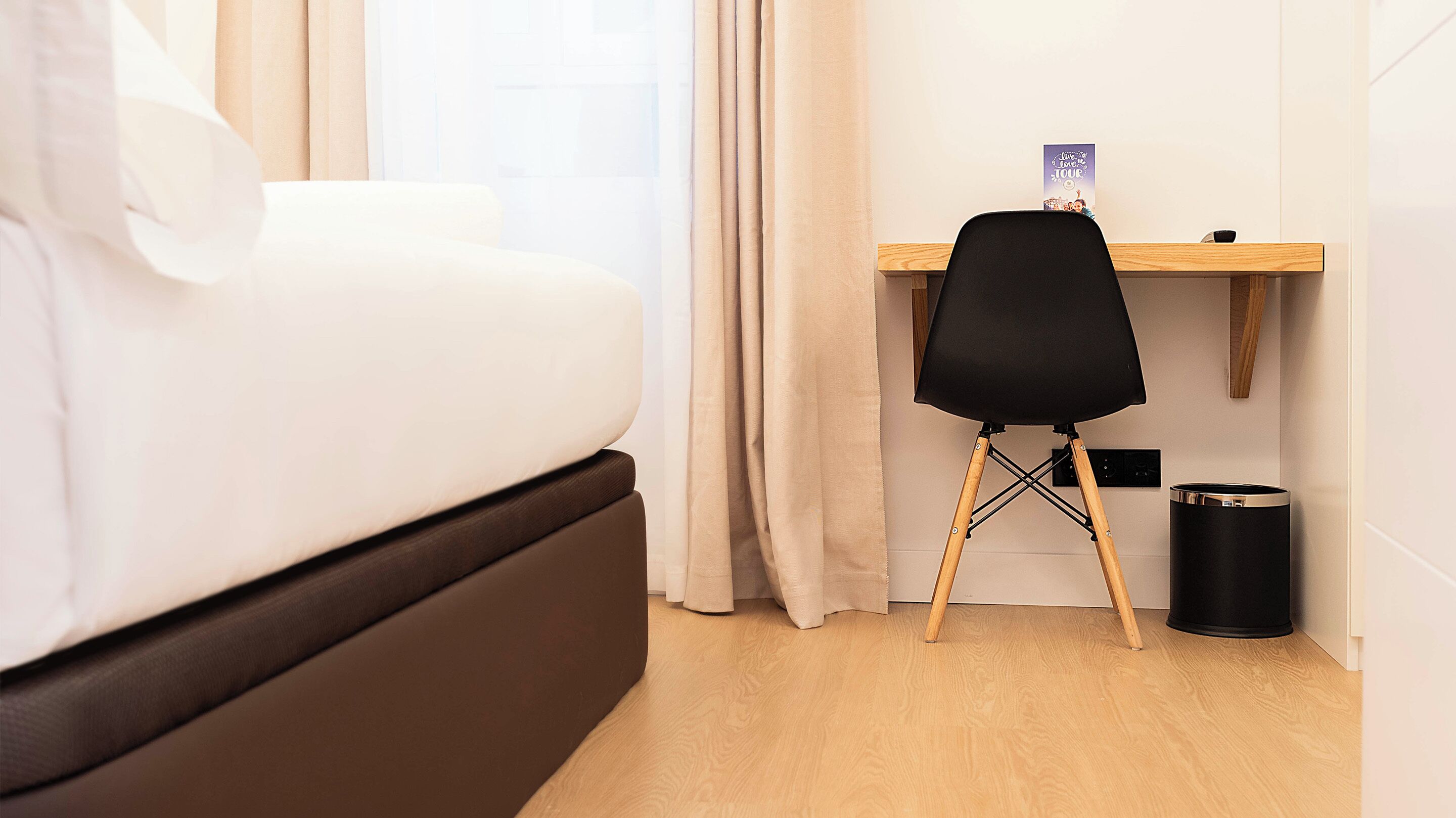 A bedroom with a bed, a desk, a chair, and a trash bin.