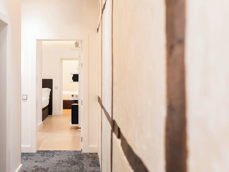 Ein Flur, der in ein Schlafzimmer mit Bett, Nachttisch und Beistelltisch führt.