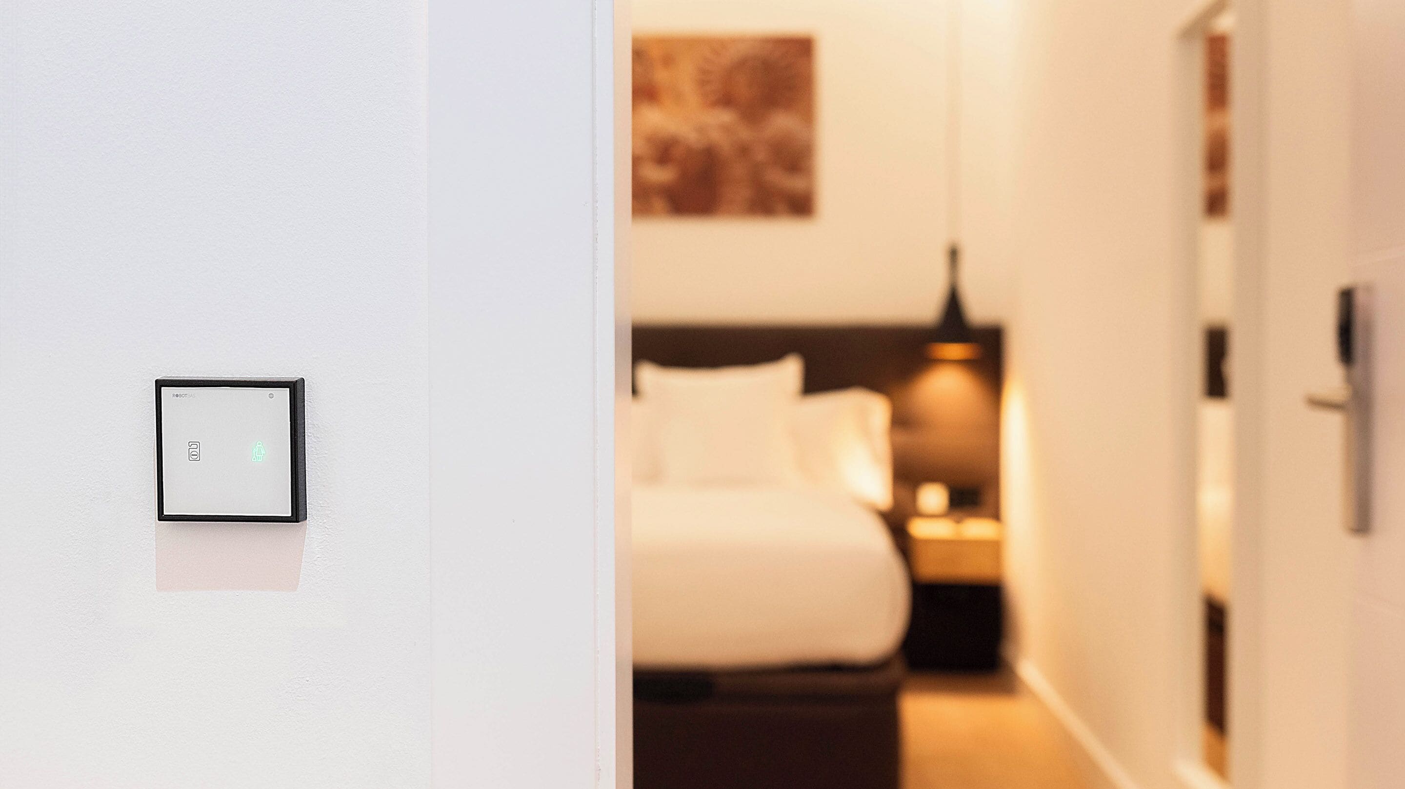 A hotel room with a bed, bedside table, and a wall-mounted light fixture.