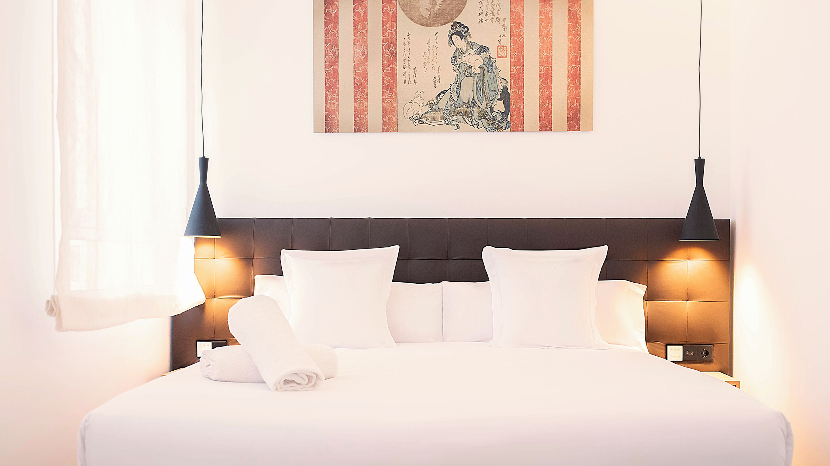 Un lit bien fait, avec du linge de lit blanc et des oreillers, une tête de lit sombre et deux lampes fixées au mur.