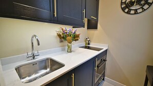 Een moderne keuken met donkere kastjes, een roestvrijstalen spoelbak en een decoratieve klok aan de muur.
