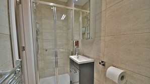 A modern bathroom with a glass-enclosed shower, a sink with a mirror, and a toilet paper holder on the wall. - The Milan Suite at Moat House (Lancashire)